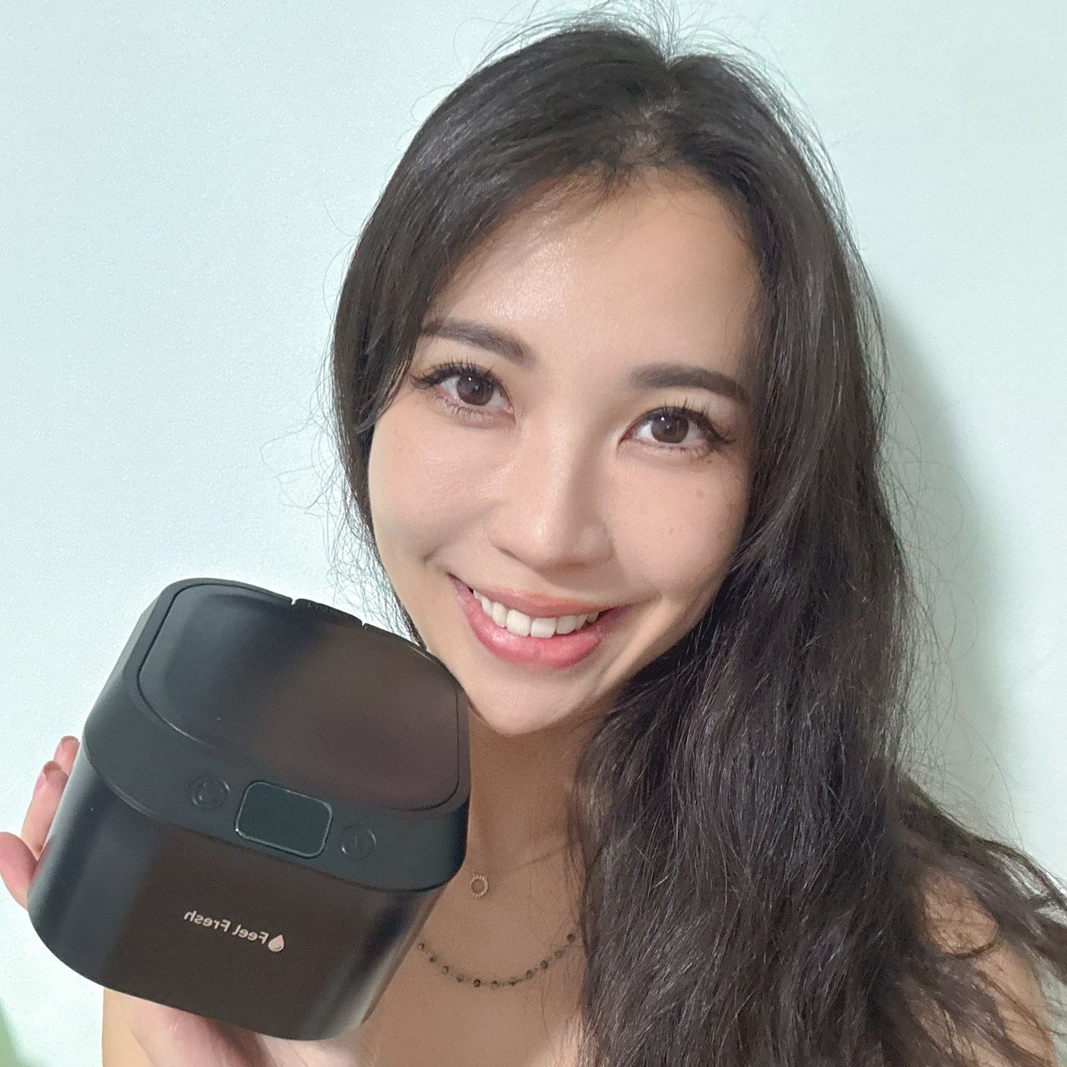 Woman holding a black device with a brand logo against a light blue background